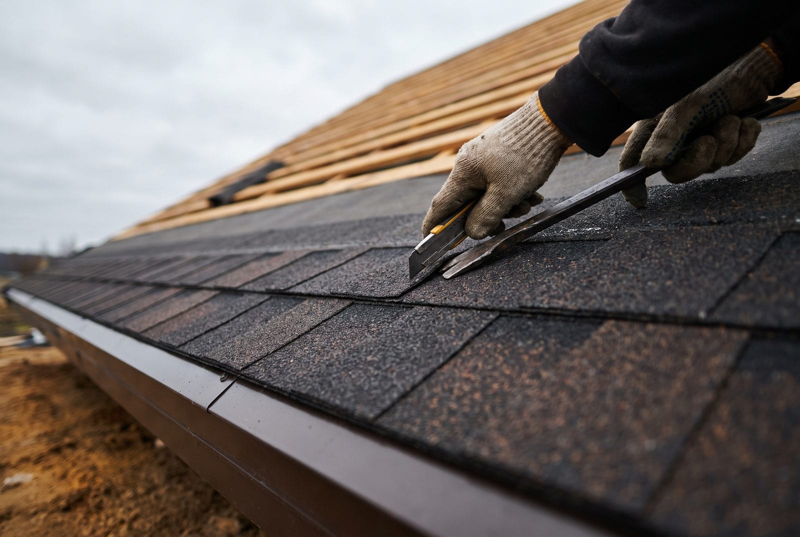 A new architectural shingle slope being finished at the eave, drip edge and starter course visible.